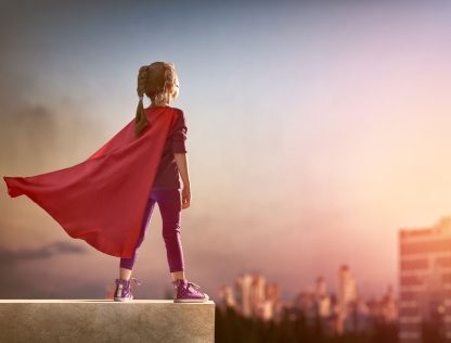 a little girl wearing a red cape standing on a ledge.