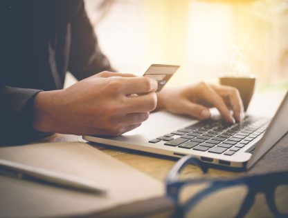 a person using a laptop computer while holding a credit card.